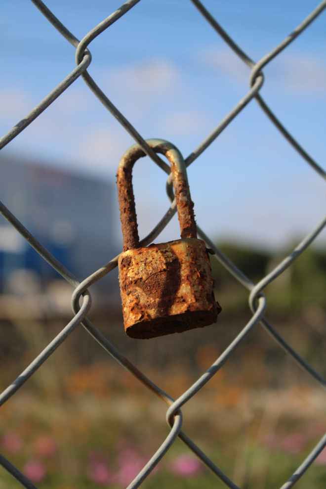A rusty padlock on a wire mesh fence a symbol of keep out forbidden territory