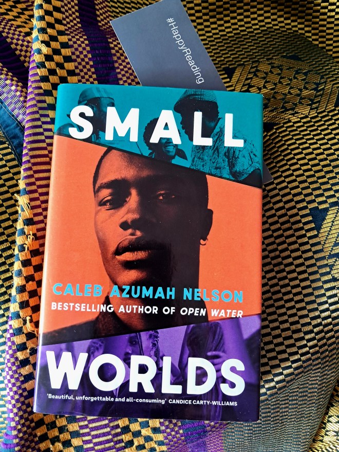 Cover of Small worlds by Caleb azumah nelson bestselling author of Open Water. The book sits on a piece of yellow, green gold Nigerian wedding fabric